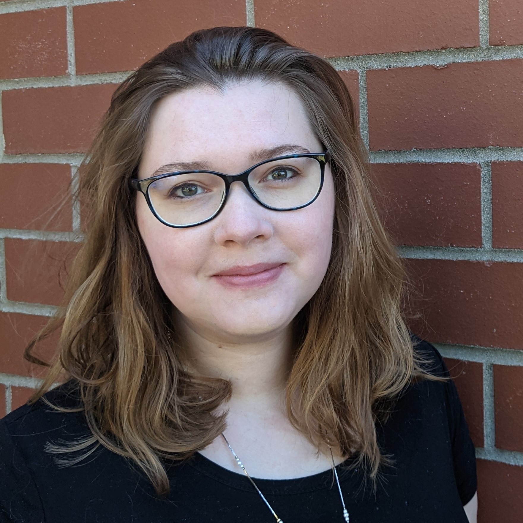A white, mid-size, female-presenting person in her mid-thirties with shoulder-length wavy hair. She wears glasses with black frames.