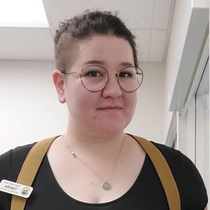 White woman with brown hair tied back wearing a black shirt and round glasses