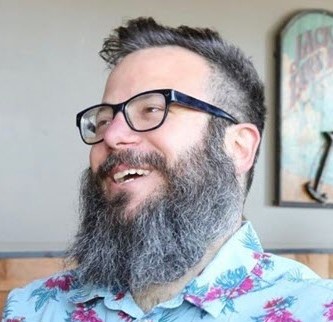 Headshot of John Pappas in a floral shirt laughing at something very funny that he just said.