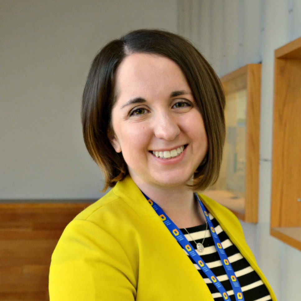 Headshot of Renee Grassi smiling at the camera wearing a yellow blazer